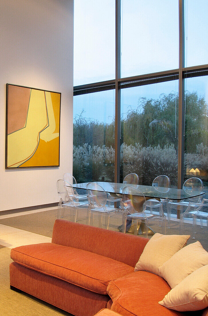 Dining area with perspex table and chairs sofa upholstered in terracotta cloth and artwork by Alberto Carbi