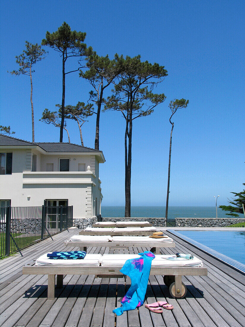 Decked poolside beach house exterior with trees and view to sea