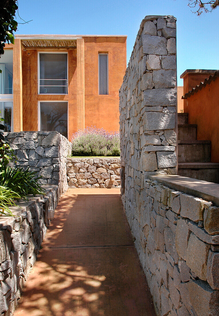 Beach house exterior viewed through pathway with stone wall
