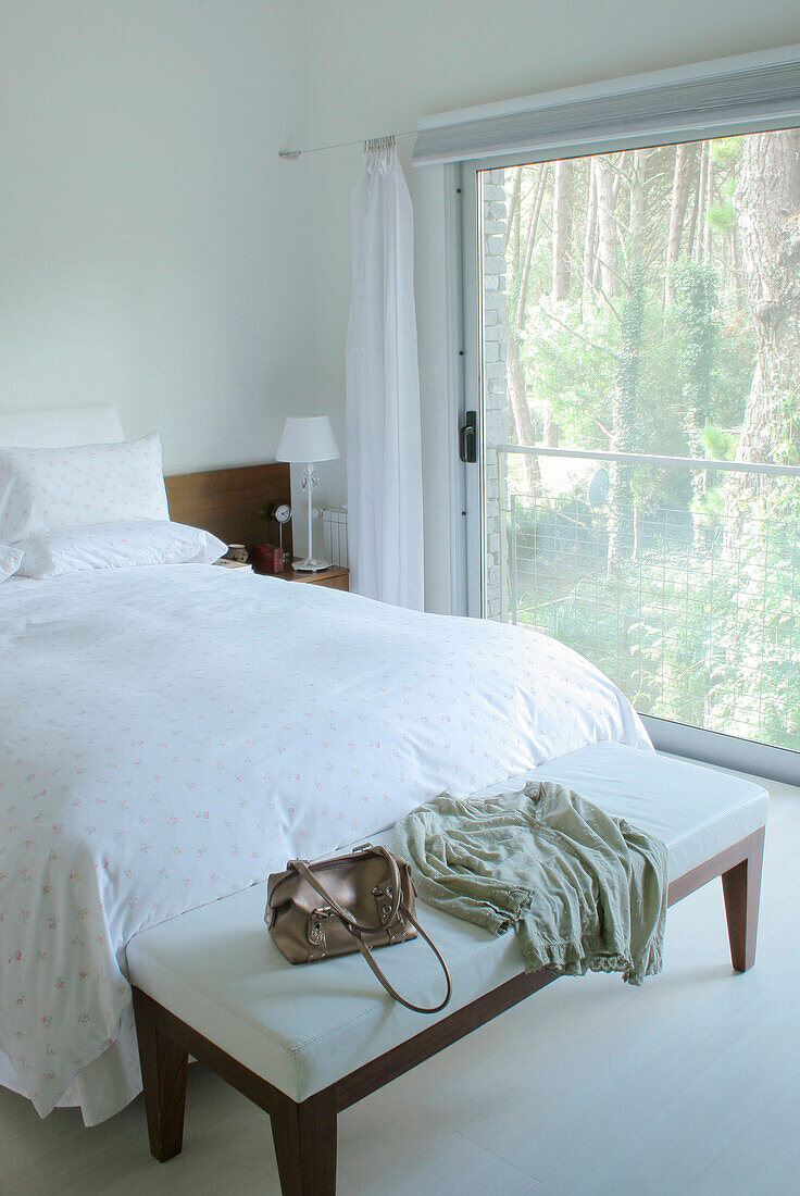 White bedroom with clothing accessories on bench seat and large sliding window