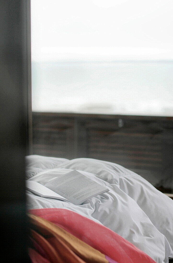 Open book on duvet of beach house with view to sea