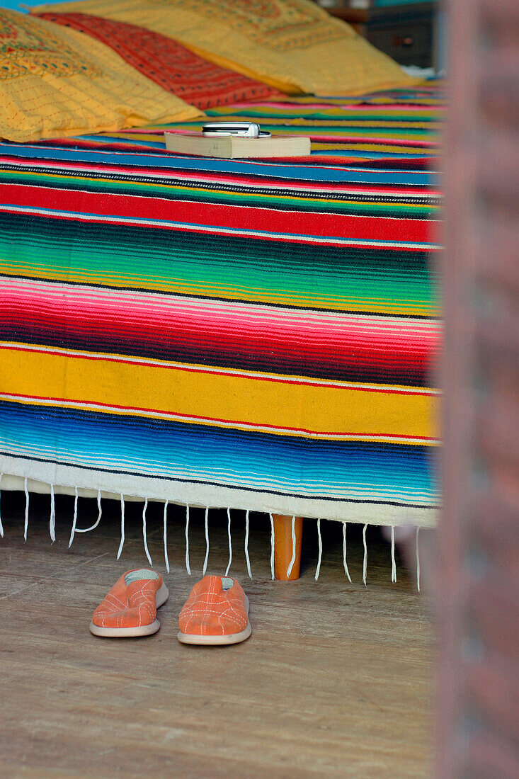 Multicoloured Mexican blanket on bed with shoes and a book