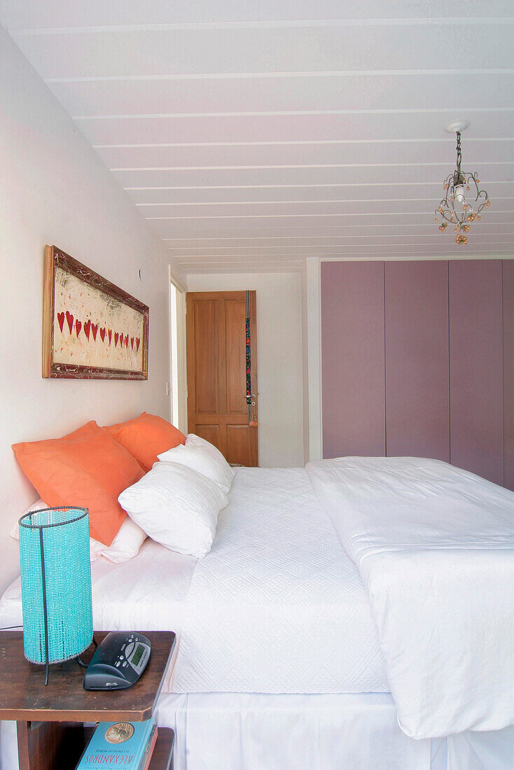 Double bed with bright orange pillows with turquoise lamp on bedside table