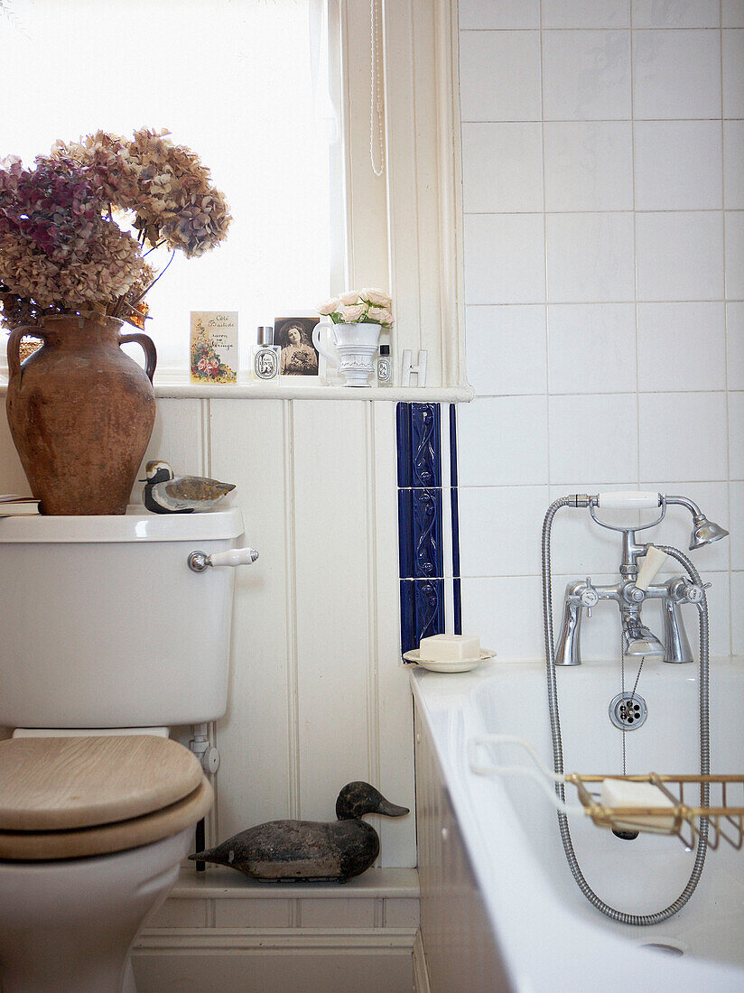 Pottery vase of dried flowers on cistern in white tiled bathroom