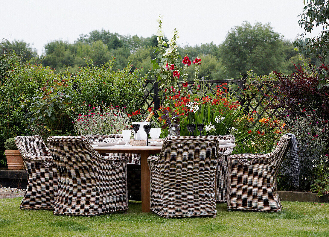 Rohrmöbel am Gartentisch mit blühenden Blumen