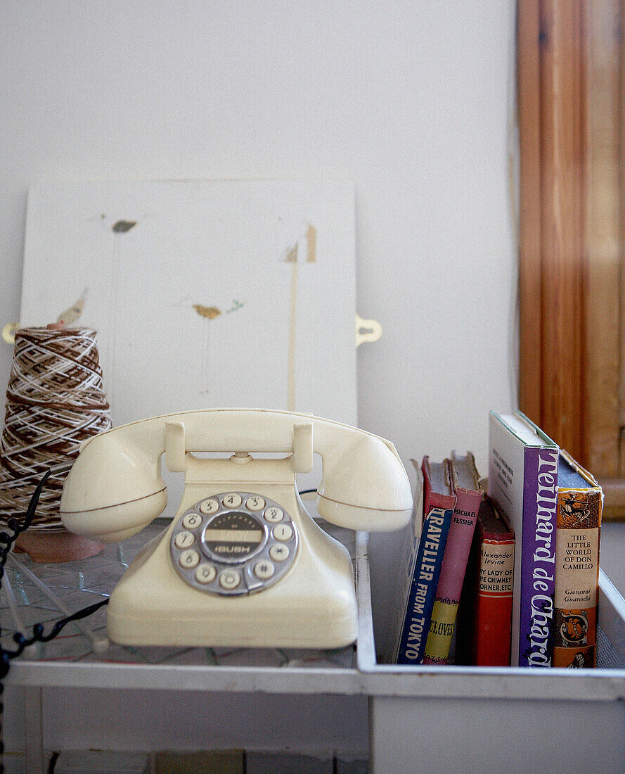 Cremefarbenes Wählscheibentelefon mit Büchern und Strickspule