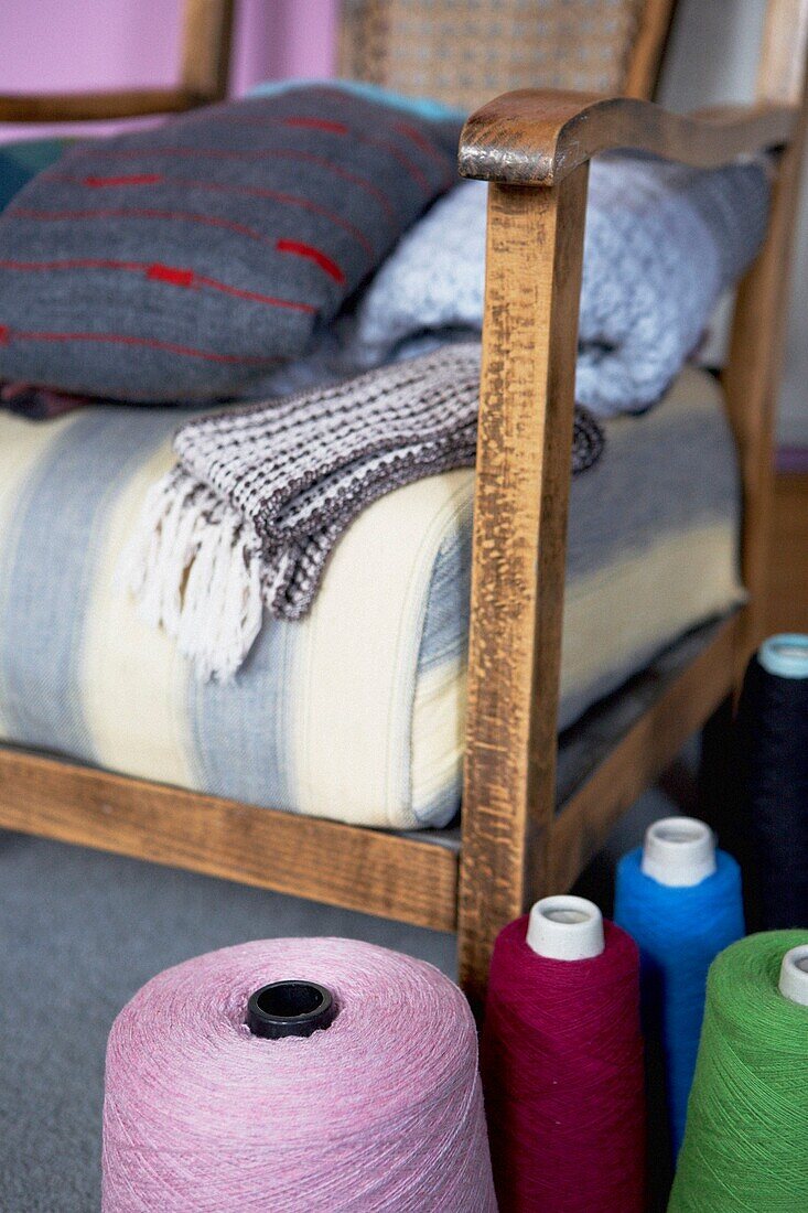 Blankets on wood framed armchair with spools of wool