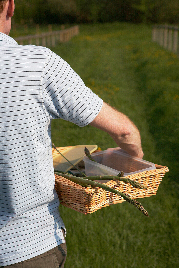 Mann geht mit einem Korb in der Hand auf ein Tor in einer Wiese in Gloucestershire zu