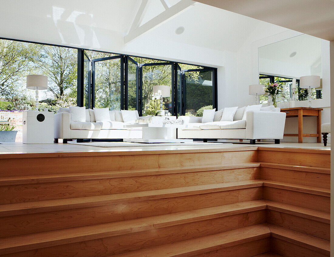 Open plan living room with white furniture and wooden steps