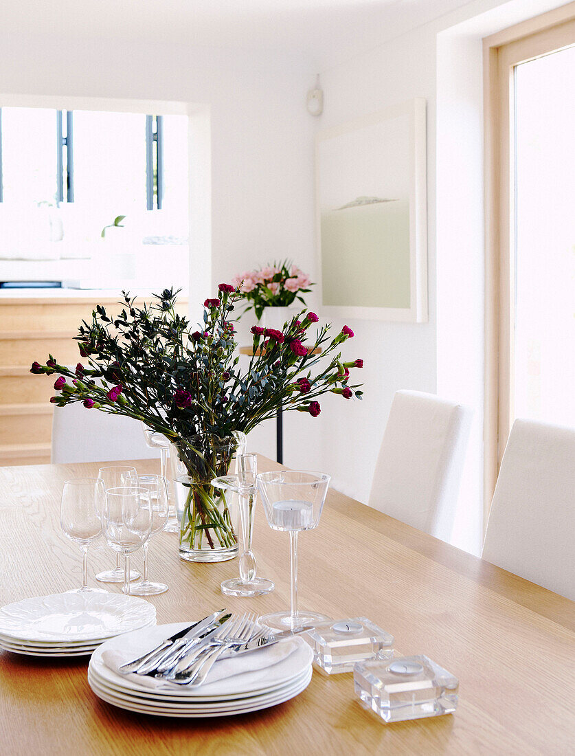 Cut flowers and tableware on wooden dining table