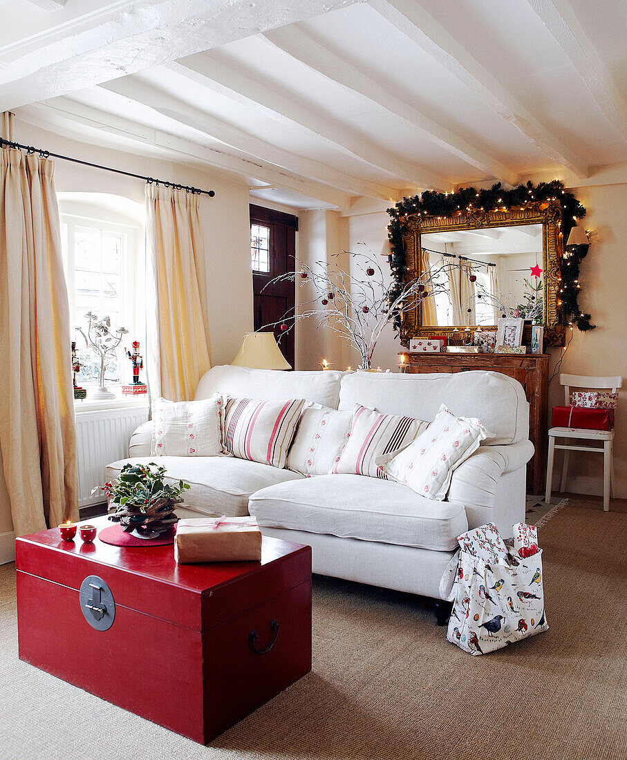 White two seater sofa and red chest in reception room with fairy lights and garland over gilt framed mirror