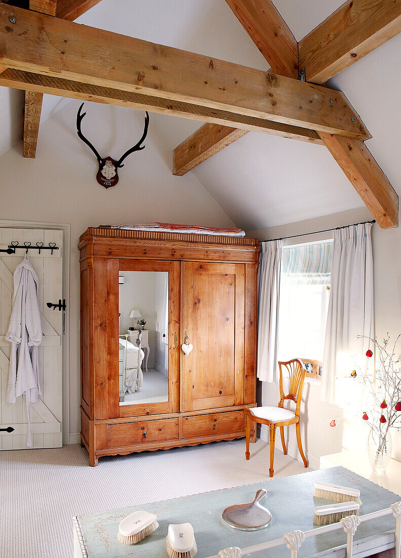 Hairbrushes and hand mirrors on dressing table in beamed bedroom with wooden wardrobe