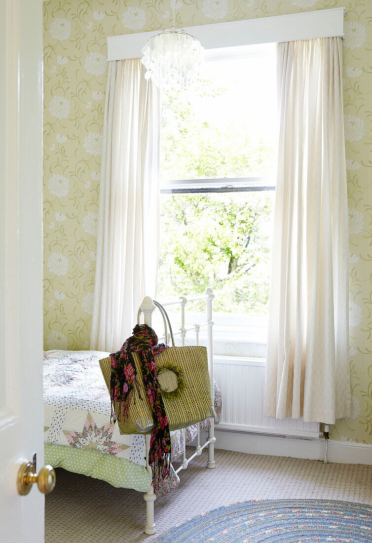 Shopping bag and scarf hang on footboard of single bed at sunlit window