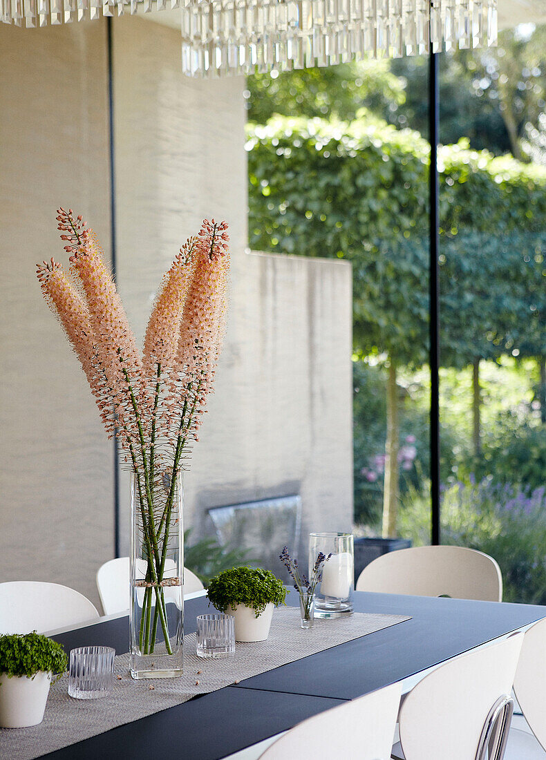 Schnittblumen auf einem Esstisch mit Blick durch eine Glaswand auf den Garten