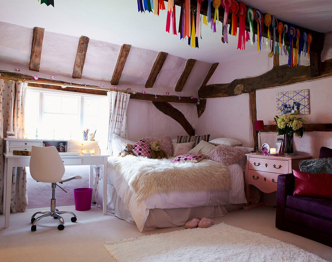 Desk and chair at window of beamed girls bedroom