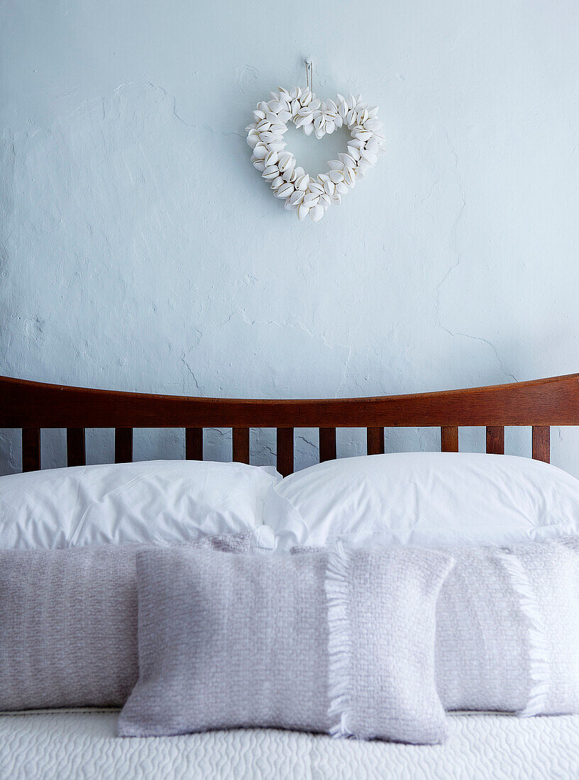 Pastellfarbene Kissenbezüge auf einem Holzbett mit herzförmigem Ornament