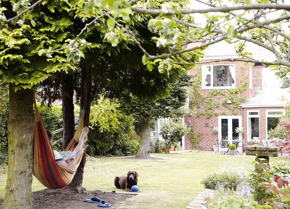 Person lying in hammock with dog nearby in garden of Gateshead home Tyne and Wear England UK