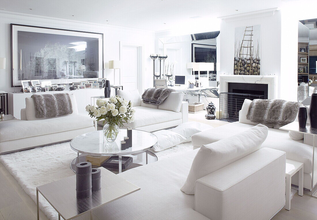 Circular coffee table and modern art in seating area of white mirrored living room in London home UK