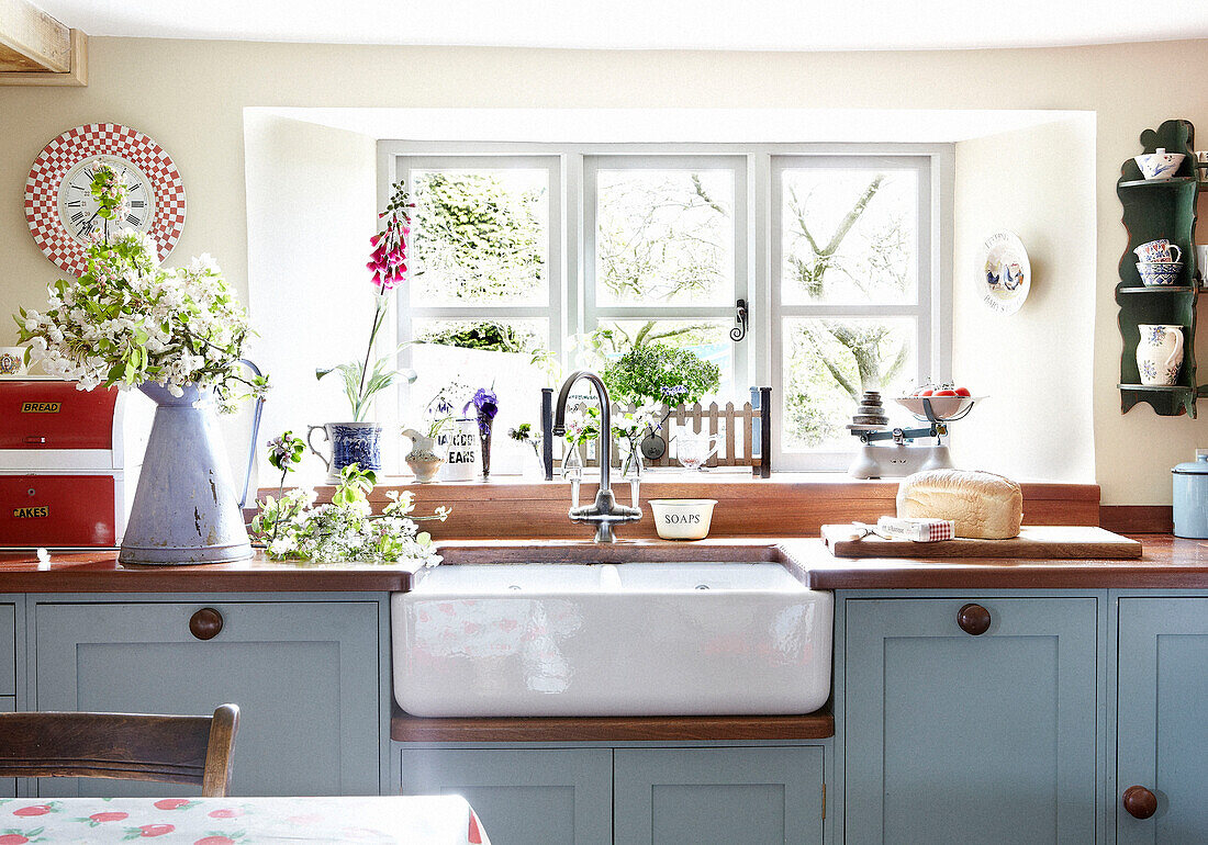 Cut flowers on wooden counter beside sink at sunlit window in Oxfordshire cottage, England, UK