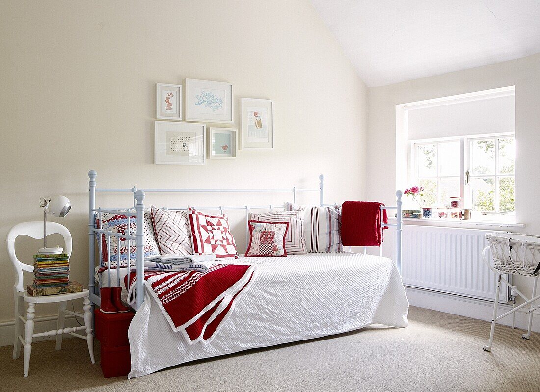 Blaues Daybed mit roten Kissen und Decken unter einem Kunstwerk in einem modernen Haus in Staffordshire, England, UK
