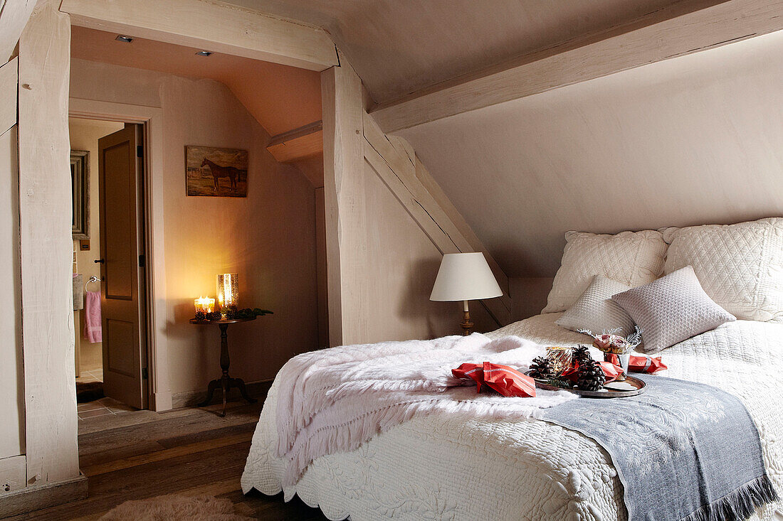 Wolldecken und Kissen auf einem Dachbodenbett mit Blick auf einen mit Kerzen beleuchteten Beistelltisch in einem festlichen Haus in Oxfordshire, England, Vereinigtes Königreich