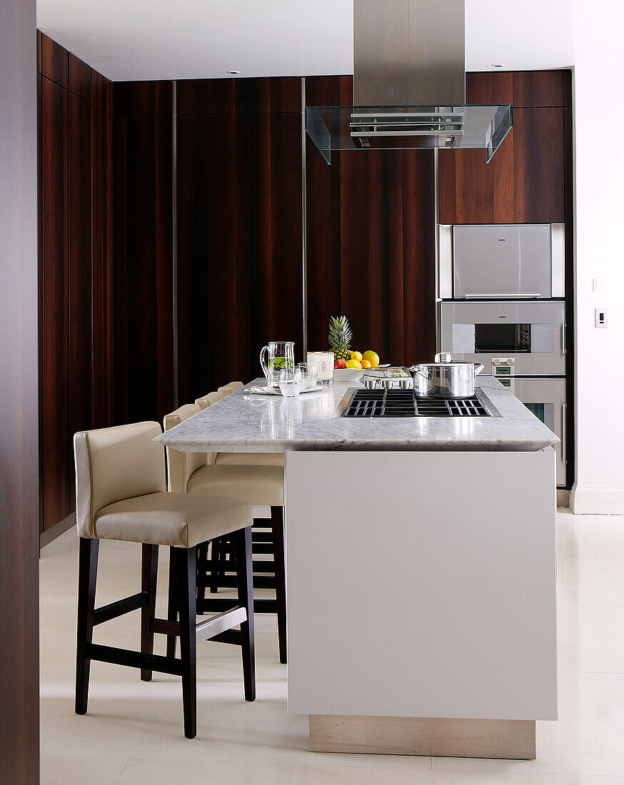 Cream leather barstools at breakfast bar in classic dark wood London kitchen, England, UK