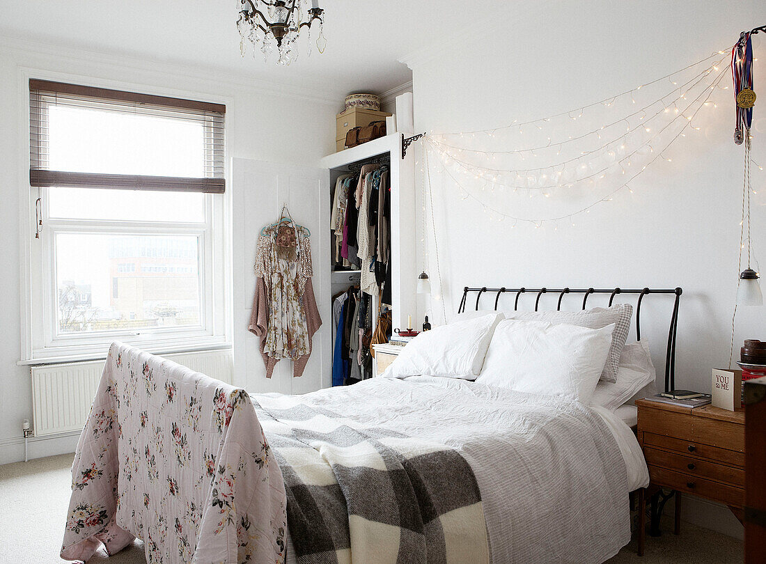 String of lights above unmade bed with grey checked blanket and floral quilt in contemporary home, Hastings, East Sussex, UK