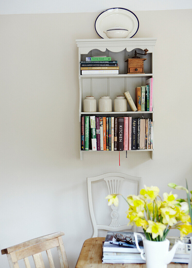 Wandgebundenes Bücherregal mit Geschirr und Narzissen in einem Haus in Warwickshire, England, UK