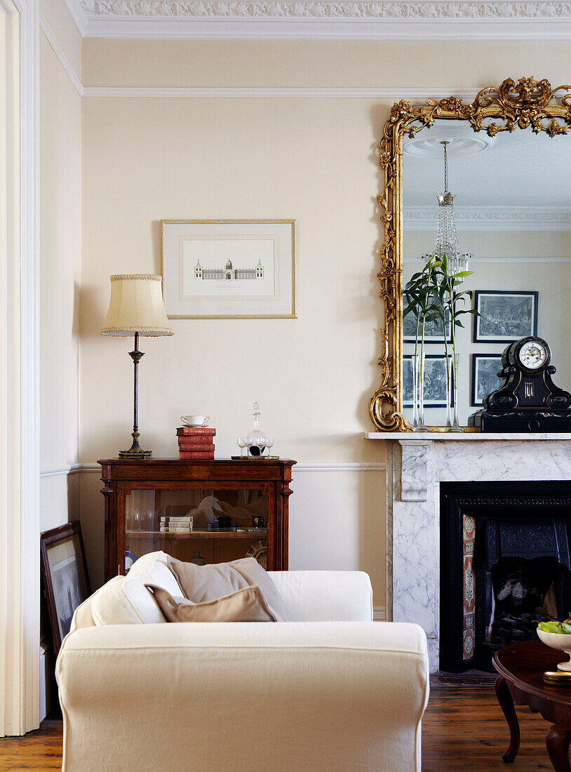 Antiker vergoldeter Spiegel auf Marmorkamin im Wohnzimmer mit cremefarbenem Zweisitzer-Sofa in einem Haus in Warwickshire, England, UK