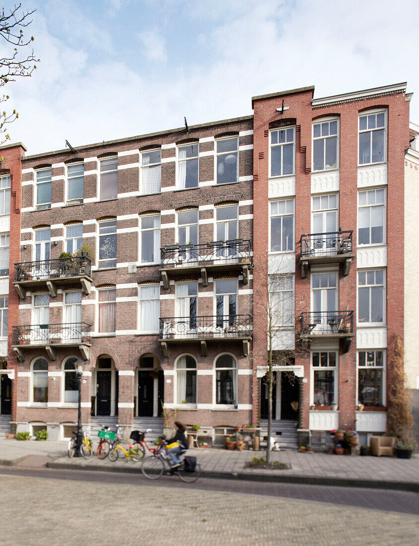 Woman cycling past brick apartment building in Amsterdam, Netherlands