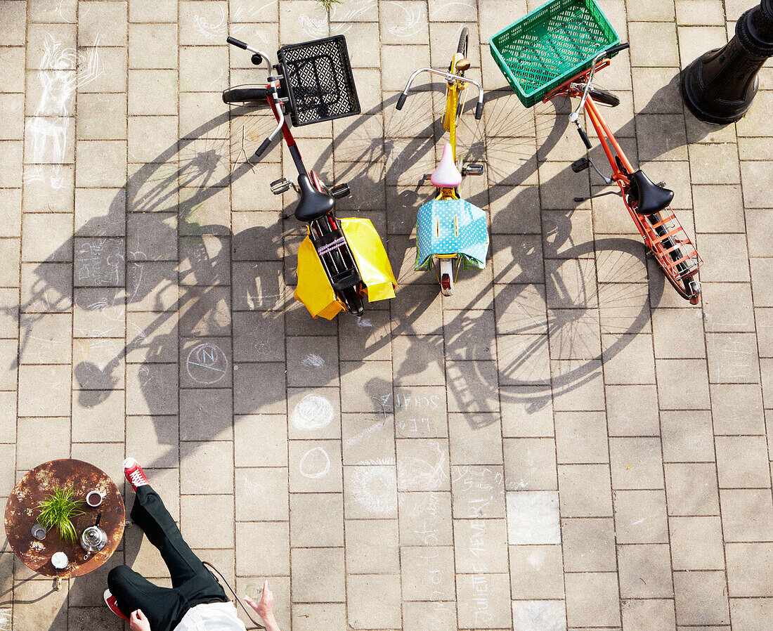 Mann sitzt in einem Straßencafé mit geparkten Fahrrädern auf der Straße, Amsterdam, Niederlande