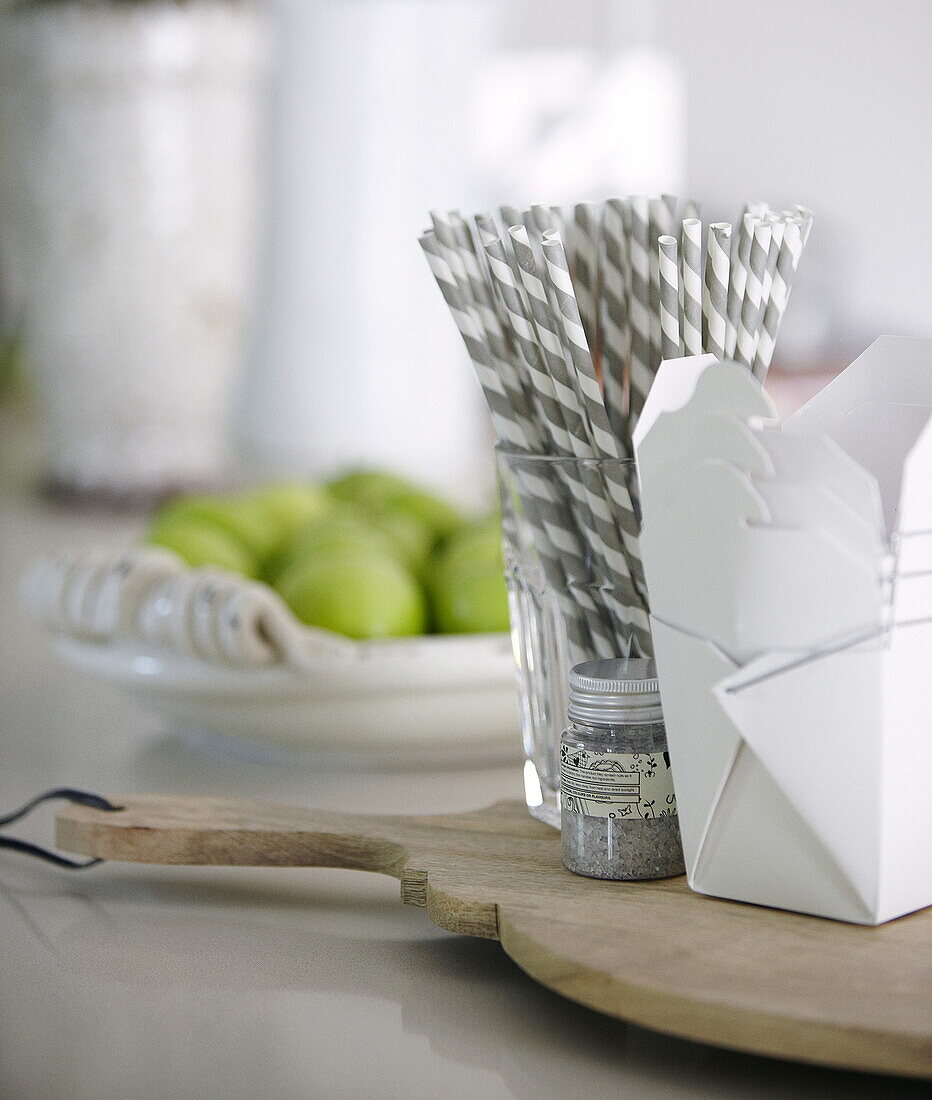 Grey striped drinking straws with takeaway food boxes on chopping board with apples, Oxfordshire, England, UK