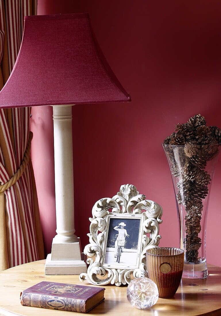 Rote Lampe und Tannenzapfen in Vase mit Vintage-Foto auf hölzernem Beistelltisch, Oxfordshire, England, Vereinigtes Königreich