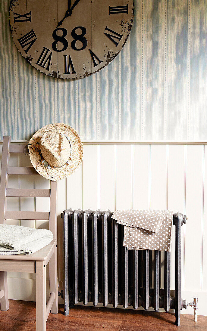 Sunhat on back of chair next to radiator below large clock with roman numerals, North London home, England, UK