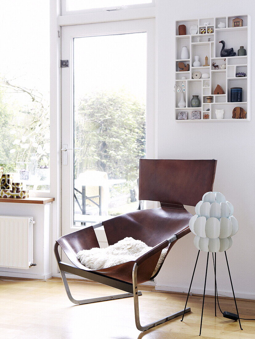 Retro-Sessel aus braunem Leder mit wandmontiertem Regal an der Glasrückwand in einem Haus in Bussum, Niederlande