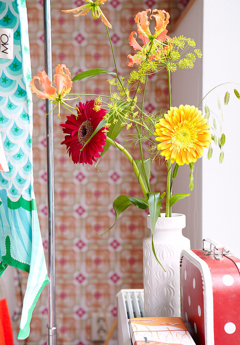 Rote und gelbe Gerbera in Vase mit gepunktetem Koffer in einem Haus in der Mattenbiesstraat, Niederlande