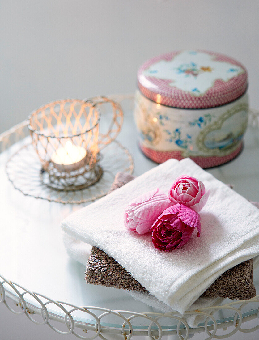 Pink flower heads and lit candle with metal tin on side table in Derbyshire farmhouse England UK