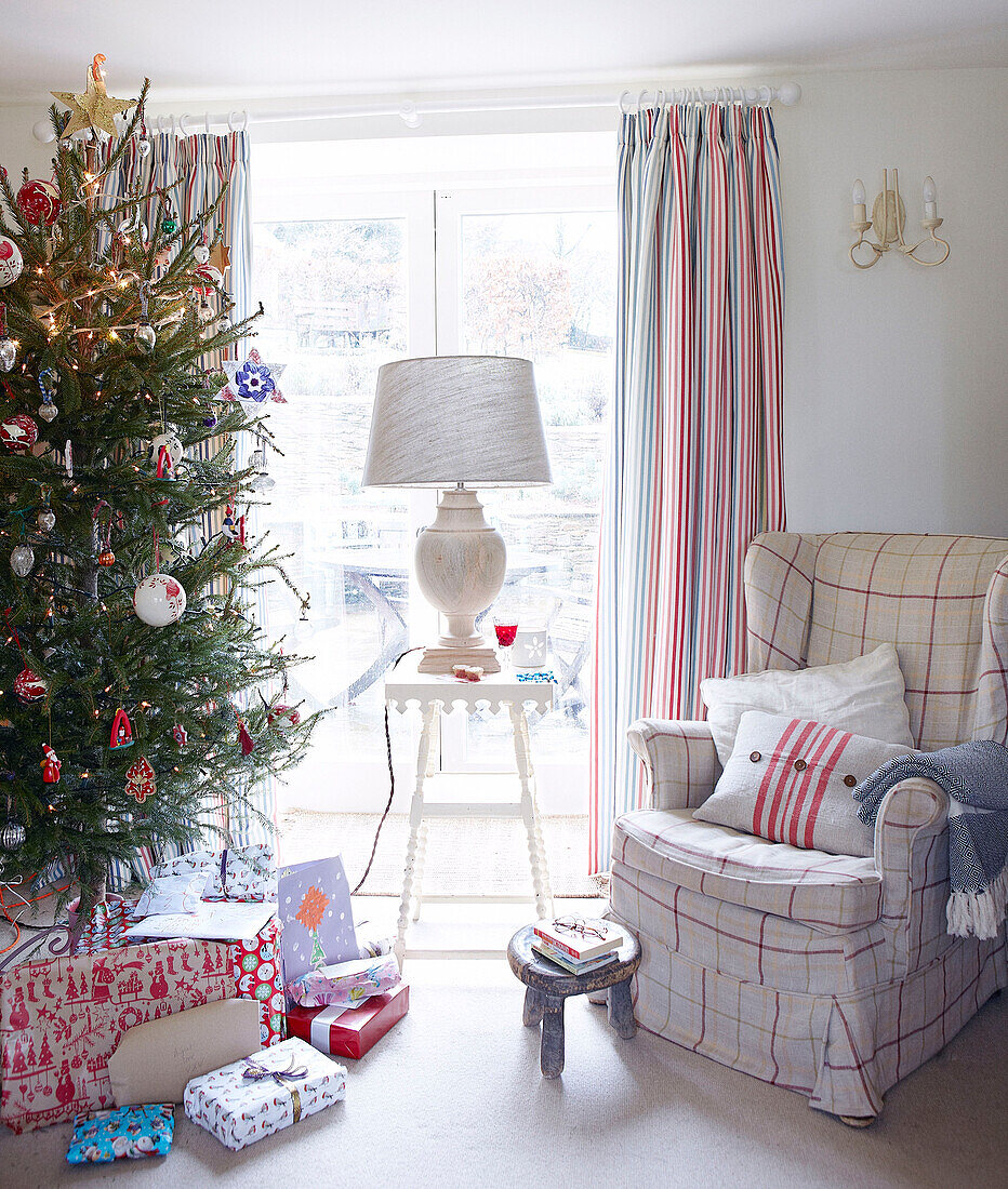 Christmas tree and armchair with lamp on table at window of Devonshire country home UK