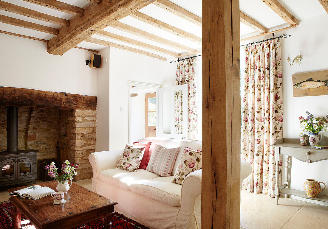 Weißes Sofa mit Couchtisch und Holzofen in freiliegendem Ziegelsteinkamin in einem Fachwerkhaus in Oxfordshire, England UK