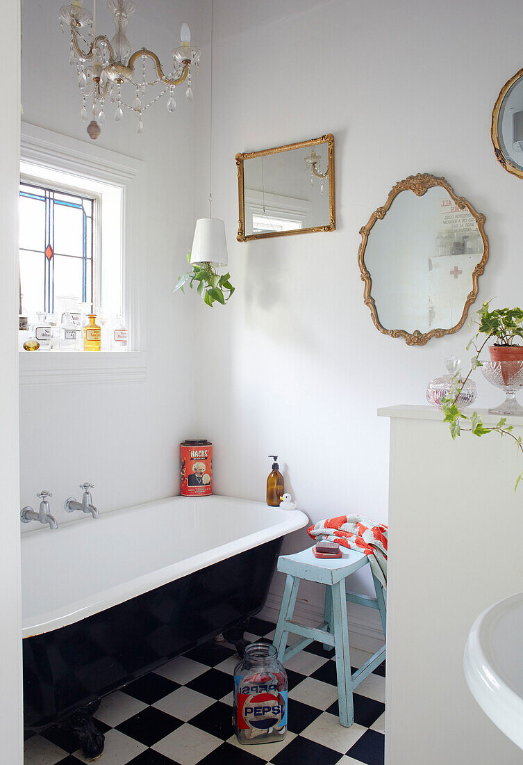 Rolltop bath below stained glass window with vintage gilt-framed mirrors in Auckland home North Island New Zealand