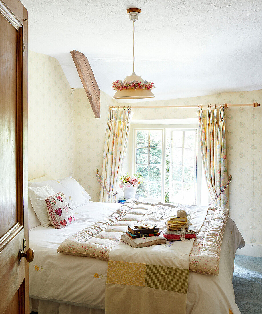 Books and ribbon on quilt in sunlit bedroom of Devonshire cottage UK