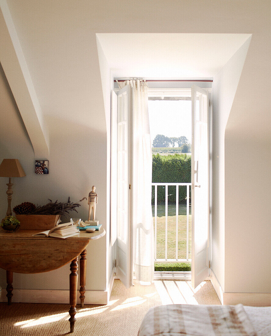 Klapptisch neben den offenen Balkontüren eines bretonischen Gästehauses in einem Schlafzimmer in Frankreich