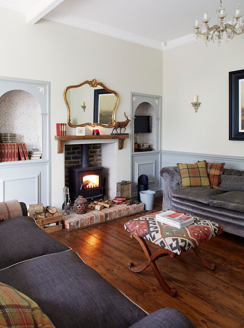 Befeuerter Kaminofen mit grauen Sofas und poliertem Holzboden in einem Haus in der Grafschaft Durham, England UK