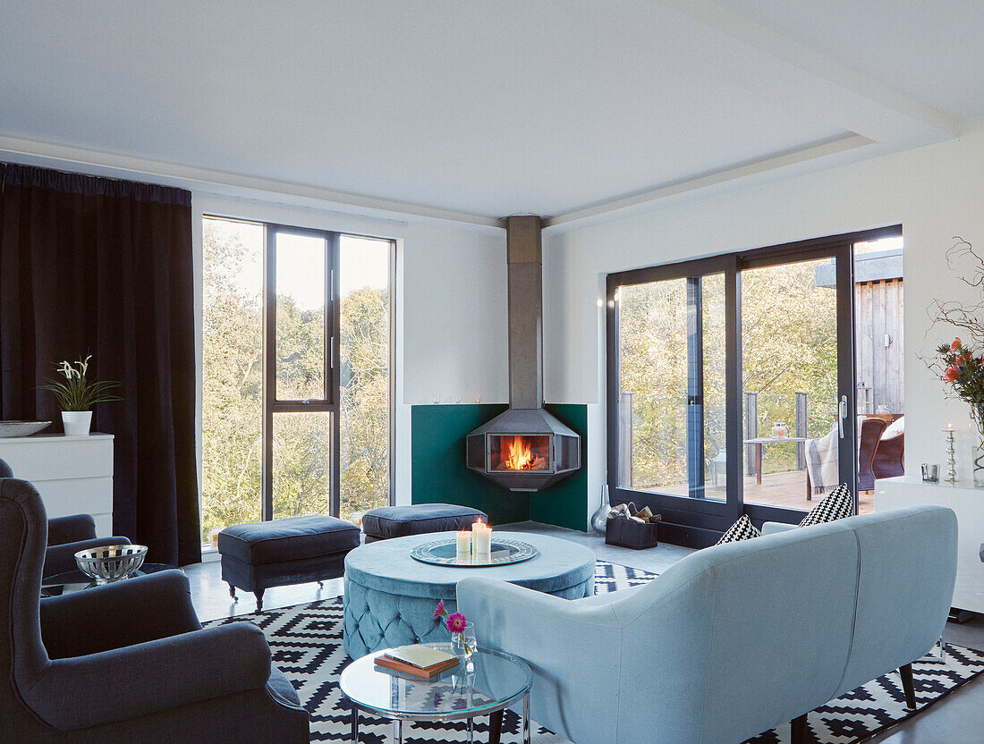 Armchairs and sofa with lit fire at doorway to balcony of 19th Century Grain Mill conversion Scottish Borders, UK