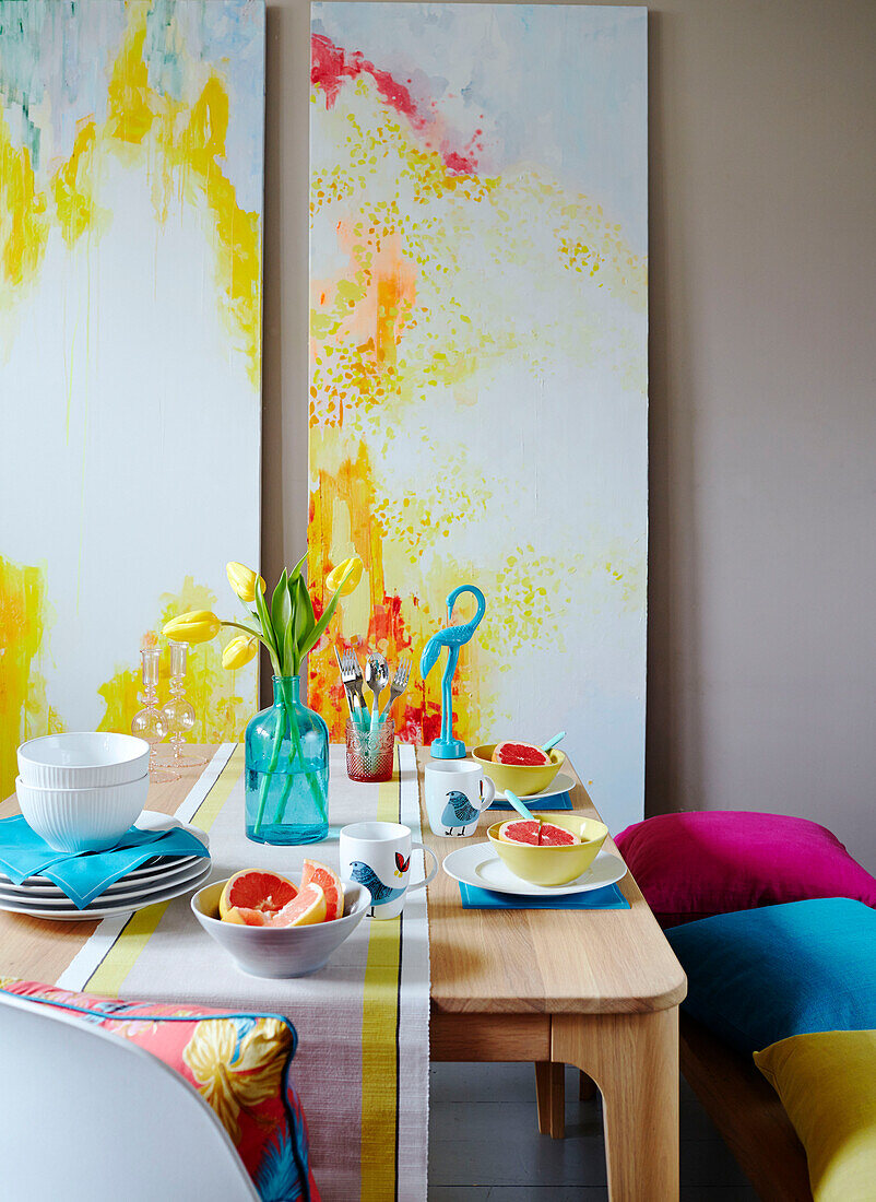 Cut tulips with grapefruit in bowls and modern artwork on dining table with cushions in studio,, UK