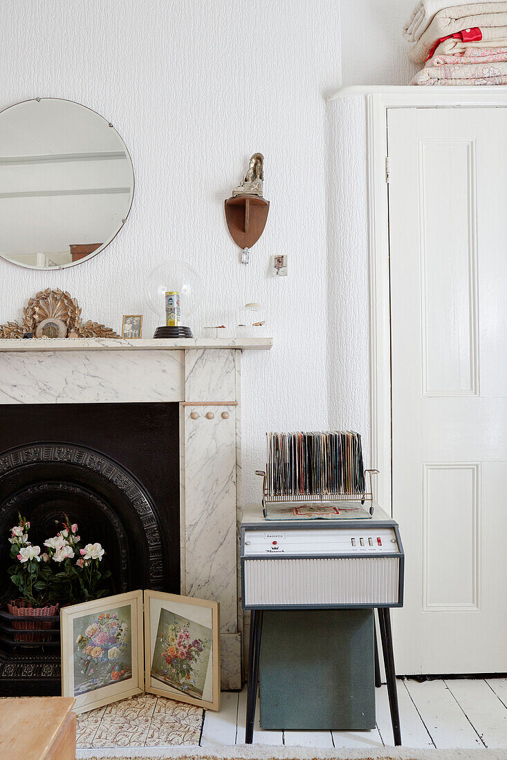 Runder Spiegel über einem Marmorkamin mit Plattenspieler und Schallplatten in einem Schlafzimmer in einem Landhaus in Durham, Nordostengland