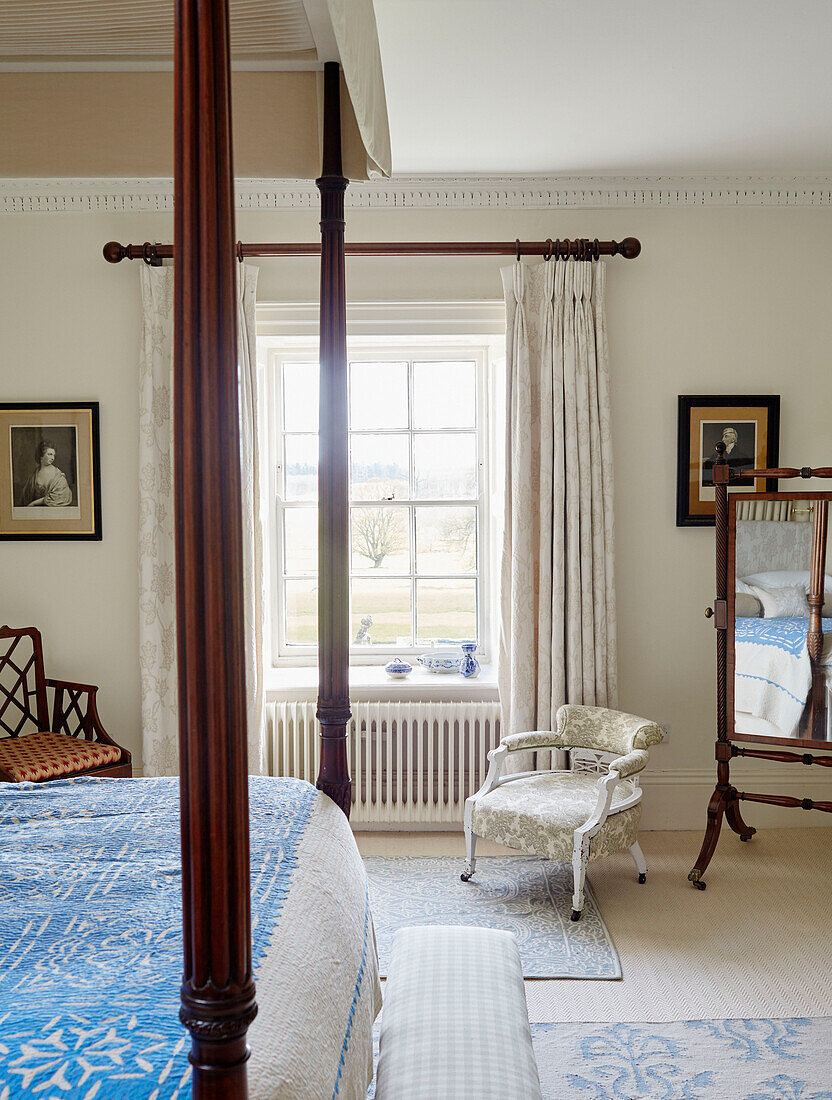 Low armchair at window of bedroom with four-postered bed in Capheaton Hall, Northumberland, UK