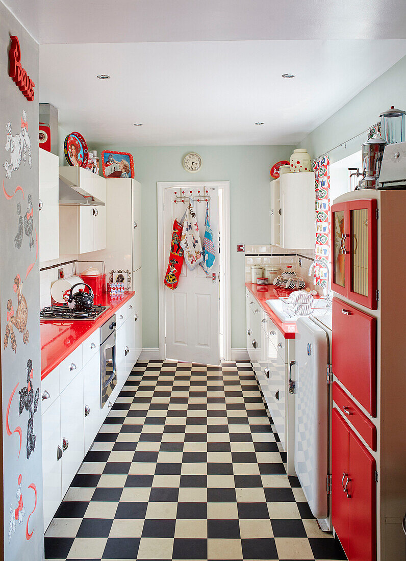 Red and white 1950s style kitchen with black and white floor in County Durham home, North East England, UK