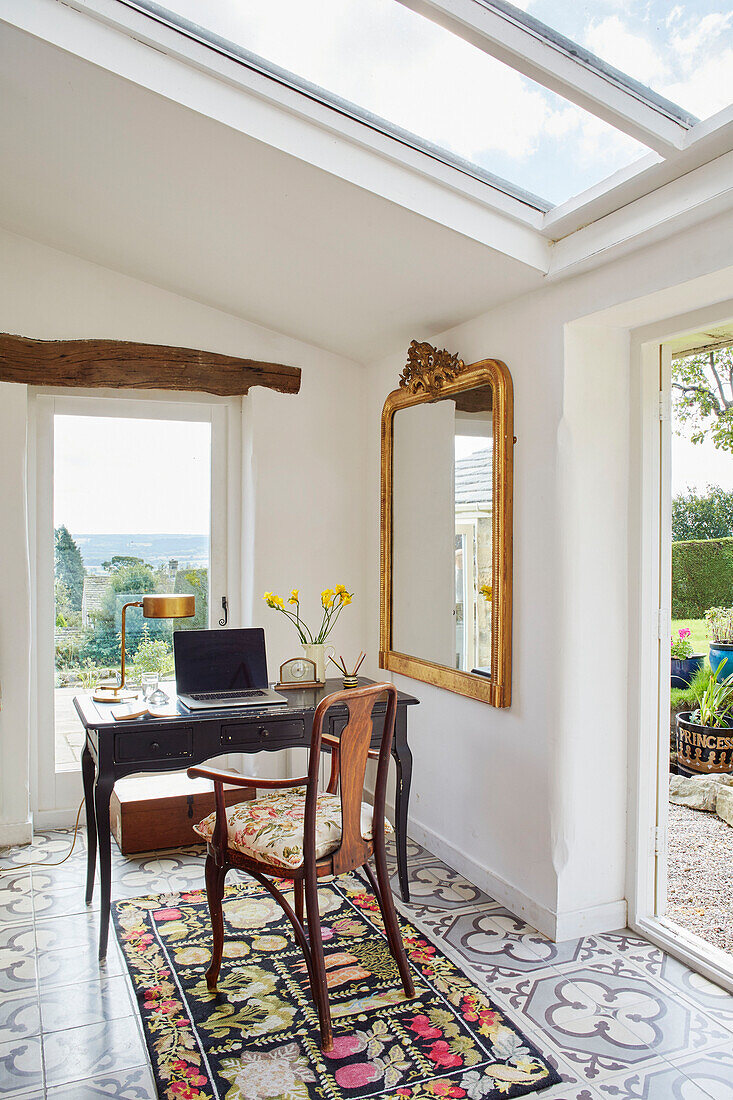 Laptop on desk with vintage chair and gilt framed mirror at window with open door in Yorkshire home, England, UK