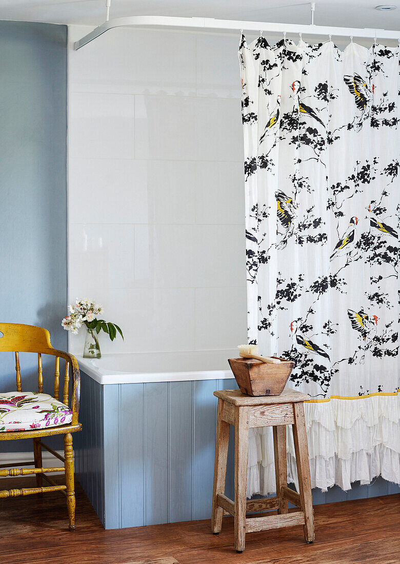Patterned shower curtain and wooden stool with blue panelled bath in Deddington home, Oxfordshire, UK